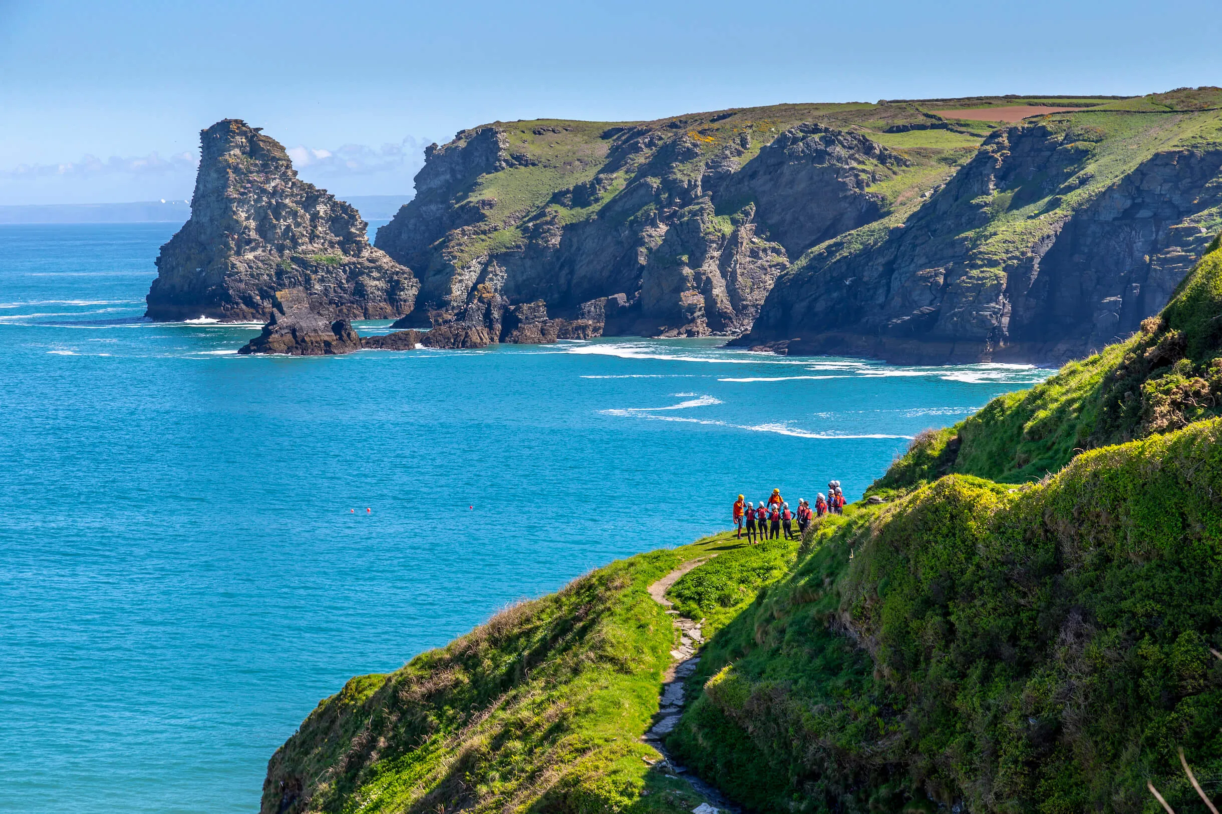 coasteer group discussing coasteering on the cliff top with the beach in the background